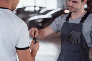 il meccanico consegna le chiavi al proprietario dell'auto riparata in officina foto