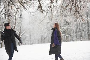 l'uomo lancia una palla di neve. splendida giovane coppia che gioca e nella foresta d'inverno foto