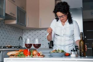 bastano poche mosse e sarà pronto da mangiare. donna in camicia bianca che prepara il cibo in cucina usando le verdure foto