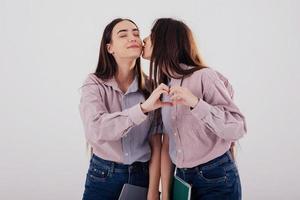 legami familiari. la ragazza dà un bacio. due sorelle gemelle in piedi e in posa in studio con sfondo bianco foto