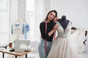 appoggiandosi al manichino. stilista femminile lavora sui nuovi vestiti in officina foto