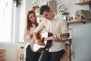 performance per una donna a casa. giovane chitarrista che suona una canzone d'amore per la sua ragazza in cucina foto