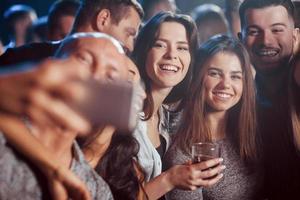 tutti mostrano i denti. amici che prendono selfie in una bellissima discoteca. con le bevande in mano foto