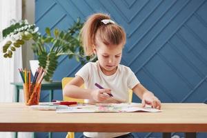 vista frontale. la bambina carina della scuola d'arte disegna i suoi primi dipinti con matite e pennarelli foto