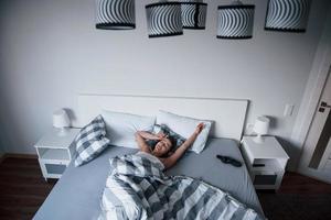 camera elegante. la donna con la maschera per gli occhi per dormire è sdraiata sul letto al mattino foto