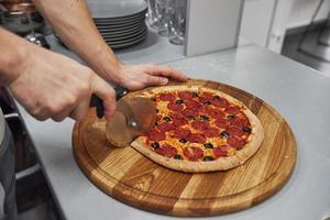 affettare a pezzi. immagine di una deliziosa pizza preparata con anelli di salsiccia e olive foto