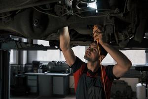 difficile vedere alcune cose l'uomo in officina in uniforme ripara le parti rotte dell'auto moderna foto