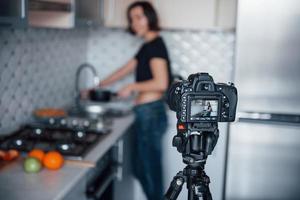fotocamera professionale su treppiede. ragazza nella cucina moderna a casa durante il fine settimana al mattino foto