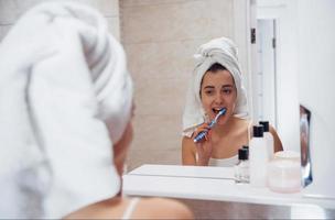 routine quotidiana con la pulizia dei denti. nel bagno. la donna in asciugamano bianco in testa si prende cura di se stessa foto