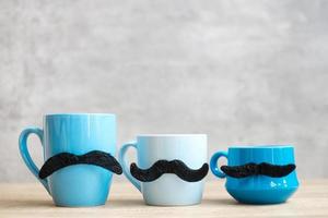 tazza di caffè blu e tazza da tè con decorazioni di baffi neri su sfondo tavolo in legno al mattino. novembre blu, felice festa del papà e concetto di giornata internazionale degli uomini foto