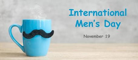giornata internazionale degli uomini con tazza di caffè blu o tazza da tè e decorazioni di baffi neri sul tavolo. felice festa del papà e concetto di celebrazione foto