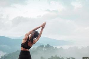 giovane donna che fa yoga e allunga i muscoli al mattino, meditazione ragazza sana contro vista sulle montagne. concetti di benessere, fitness, vitalità, esercizio e vita lavorativa foto