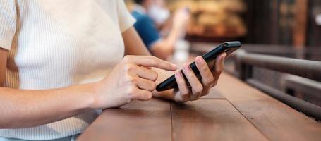 donna d'affari casual che tiene e utilizza lo smartphone per i messaggi sms, giovane donna che digita il telefono cellulare touchscreen in un bar o in un ufficio moderno. stile di vita, tecnologia, social media e concetto di rete foto