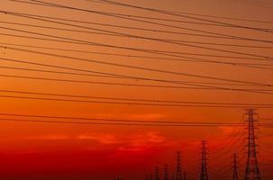 traliccio elettrico ad alta tensione e filo elettrico con cielo al tramonto. pali elettrici. concetto di fabbrica di supporto energetico ed energetico. torre di griglia ad alta tensione con cavo metallico. bellissimo cielo al tramonto rosso-arancione. foto