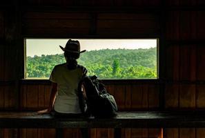 la giovane donna asiatica indossa il cappello si siede su una panca di legno e guarda la splendida vista della foresta tropicale alla torre di osservazione della fauna selvatica la sera con la calda luce del sole. concetto di viaggio della donna da solo. foto