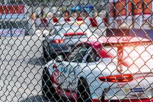 corse automobilistiche su strada asfaltata. vista dalla rete metallica del recinto sull'auto sfocata sullo sfondo della pista. super macchina da corsa sul circuito cittadino. concetto di industria automobilistica. foto