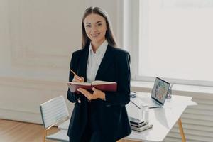 direttore femminile che tiene taccuino e matita mentre si appoggia sulla scrivania dell'ufficio foto