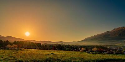 alba mattutina sulla montagna con cielo azzurro. campo in erba e pineta nel villaggio rurale vicino alla montagna rocciosa. la nebbia al mattino copriva la montagna. città in valle. prato paesaggistico foto