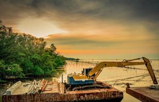 la terna sta scavando lungo la riva del mare vicino alla foresta di mangrovie per posizionare il tubo. belle nuvole e cielo al cantiere foto