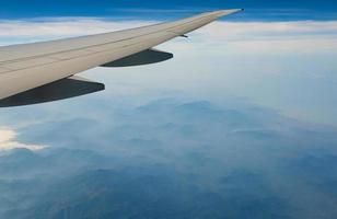 ala dell'aereo sopra la montagna. aereo che vola su cielo blu e nuvole bianche. vista panoramica dalla finestra dell'aeroplano. volo di una compagnia aerea commerciale. ala dell'aereo. concetto di meccanica di volo. volo internazionale. foto