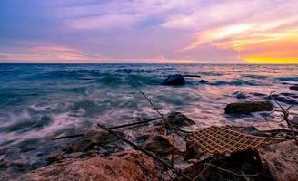 acqua di mare con cielo al tramonto dorato e viola. rifiuti di plastica sulla spiaggia rocciosa. spiaggia tropicale e inquinamento oceanico. acqua dell'oceano. mare d'estate. morbida onda al tramonto. paesaggio marino. bellezza nella natura. foto