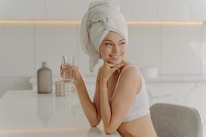 ritratto laterale di bella donna caucasica seduta in cucina con un bicchiere d'acqua foto