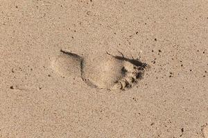 traccia di un piede nudo di un uomo sulla sabbia. stampa su una superficie bagnata sullo sfondo della spiaggia foto