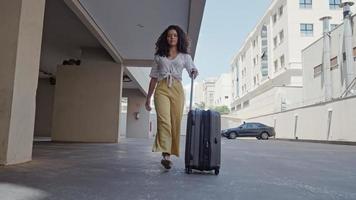 giovane turista latina cammina con una valigia su ruote in giro per la città sullo sfondo del garage dell'hotel foto