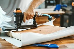 falegname che utilizza una pistola sparachiodi o una pistola a punti dopo aver sostituito un tessuto in vinile o tappezzeria sul sedile per sgabelli da bar,concetto di lavorazione del legno per il restauro di mobili. messa a fuoco selettiva foto