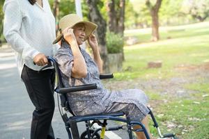 badante aiuto e cura asiatico anziano o anziano donna paziente seduta e felice sulla sedia a rotelle nel parco, sano concetto medico forte. foto