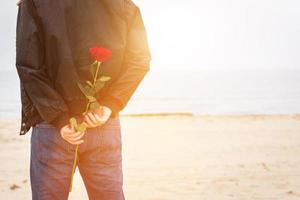 uomo con una rosa dietro la schiena in attesa di amore. appuntamento romantico sulla spiaggia foto