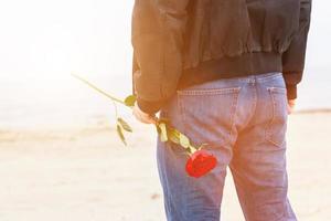 uomo con una rosa dietro la schiena in attesa di amore. appuntamento romantico sulla spiaggia foto