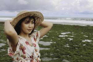 una giovane ragazza asiatica che indossa un cappello da spiaggia si sta rilassando sulla spiaggia del cielo blu a gunungkidul, in indonesia foto