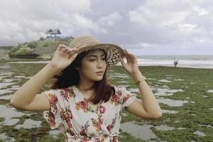 una giovane ragazza asiatica che indossa un cappello da spiaggia si sta rilassando sulla spiaggia del cielo blu a gunungkidul, in indonesia foto