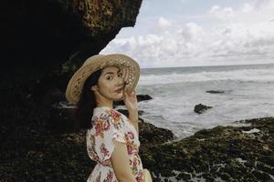 una giovane ragazza asiatica che indossa un cappello da spiaggia si sta rilassando sulla spiaggia del cielo blu a gunungkidul, in indonesia foto