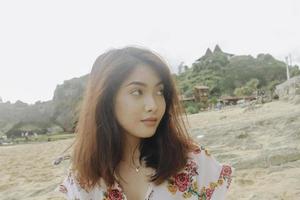 una giovane donna asiatica seduta e rilassante sulla spiaggia di sabbia, gunungkidul, indonesia foto