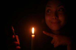 donna asiatica che sorride al suo cellulare con una candela nella notte oscura foto