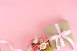 confezione regalo di carta marrone con fiocco di nastro riccio in raso rosa su sfondo rosa pastello. festa della mamma piatta, festa del papà, San Valentino, concetti di compleanno con spazio per la copia. foto