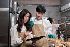 tre giovani amici e partner di avvio di pasta per il pane e pasticcini impegnati con lavori di pasticceria fatti in casa mentre cucinano ordini online, imballano e consegnano in panetteria, piccolo imprenditore foto