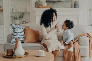 ritratto di amorevole madre incinta afroamericana che spiega al figlioletto della sua gravidanza foto