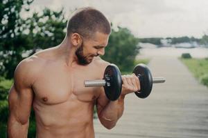 il colpo all'aperto di un uomo muscoloso forte con il torso nudo solleva il bilanciere pesante e allena i muscoli ha un allenamento per mantenersi in forma sana. il ragazzo atletico dimostra che la determinazione motiva a dedicarsi allo sport foto