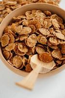 fiocchi di cereali secchi sani croccanti in una ciotola di legno con cucchiaio di legno su sfondo bianco foto