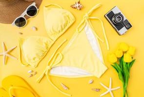 vista dall'alto di bikini e occhiali da sole con accessori da spiaggia su sfondo giallo. concetto di ora legale. foto