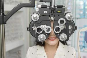 giovane cliente femminile che viene esaminata test visivo utilizzando un dispositivo di misurazione della vista con optometria bifocale da parte di un oftalmologo nel centro ottico, concetto di cura degli occhi. foto