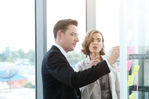 uomo d'affari di successo e donna d'affari che scrivono buone idee su note adesive incollate sulla parete di vetro in una moderna riunione d'ufficio. foto