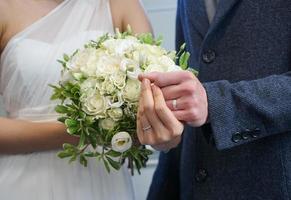 gli sposi novelli lo sposo e la sposa si stringono la mano mentre indossano l'anello e tengono i fiori calorosamente felici. durante le riprese prematrimoniali, è l'inizio di una bella vita. foto