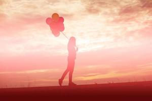 silhouette di giovane donna che tiene colorato di palloncini con il tramonto foto