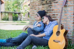 uomo hipster che suona la chitarra per la sua ragazza all'aperto contro un muro di mattoni, godendo insieme. foto