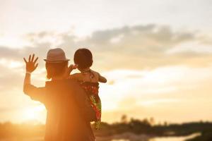 una silhouette di una bambina felice le braccia della sua amorevole madre per un abbraccio, davanti al tramonto nel cielo in una giornata estiva. foto