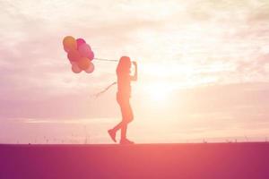 silhouette di giovane donna che tiene colorato di palloncini con il tramonto foto